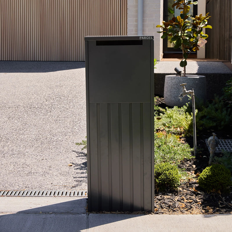 Empire Parcel Letterbox in grey steel installed beside a gravel driveway with garden planting nearby
