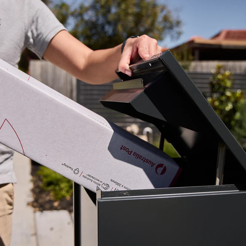 Empire Parcel Letterbox in grey steel with a person placing a parcel into the top chute outdoors