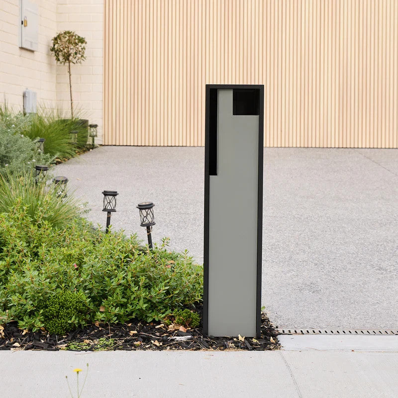 Swift Letterbox in grey installed in a garden bed beside a paved driveway, angled front view