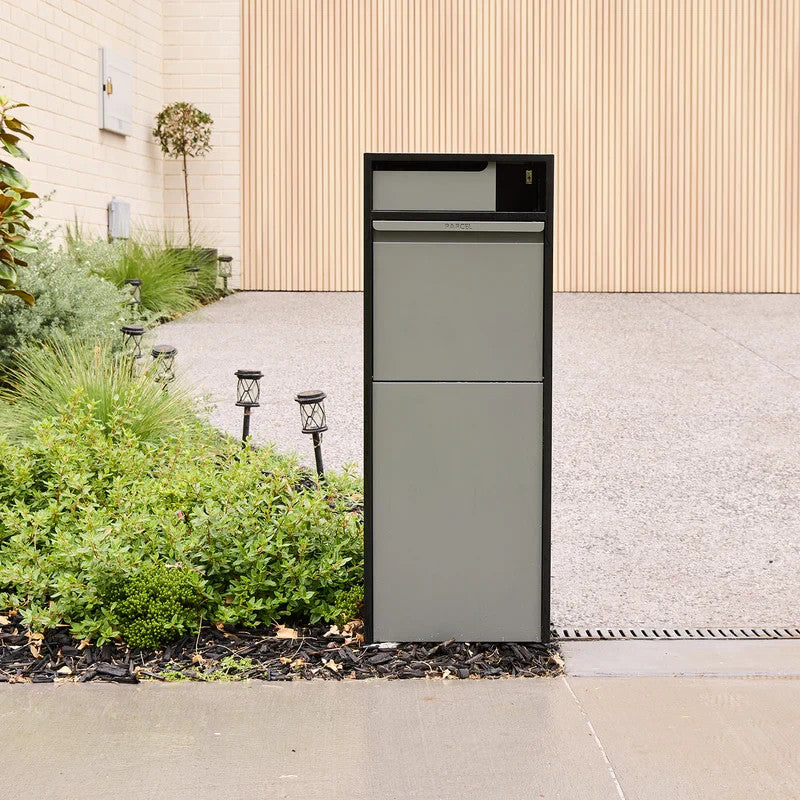 Zephyr Parcel Letterbox in charcoal steel installed beside a garden bed at the end of a paved driveway