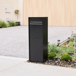 Zip Parcel Letterbox in black shown from a closer front angle beside a gravel driveway and low garden bed.